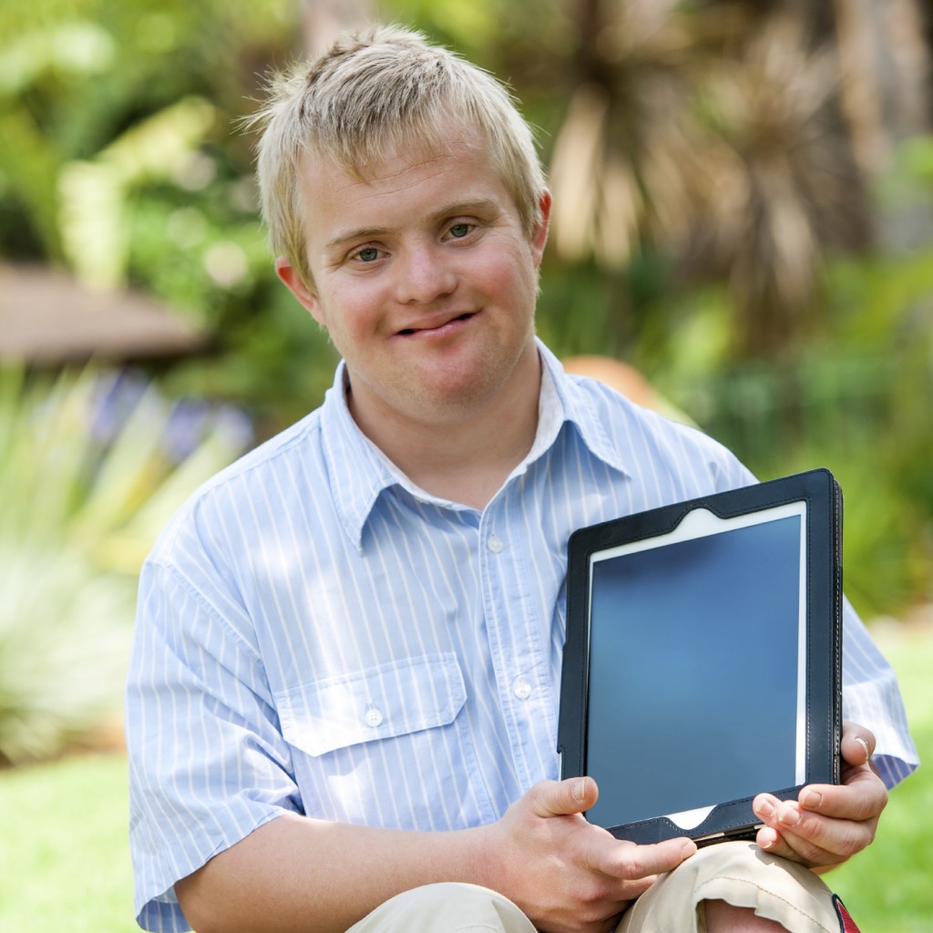 Boy with Down syndrome holding a tablet PC outdoors.