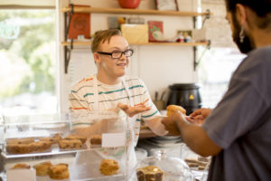 Smilende cafeansatt serverer bakeverk over disken.