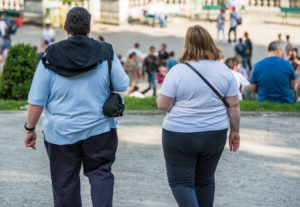 To overvektige, ganske unge mennesker spaserer i en by. De vises bakfra.