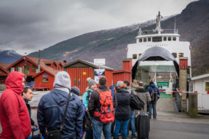 Mange mennesker i ferd med å gå ombord på en ferge i et fjellandskap.