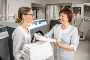 To kvinner i et vaskeri med rent lintøy i hendene