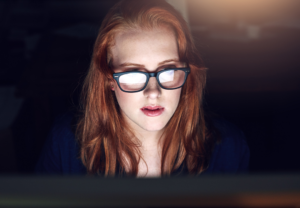 Ung kvinne foran dataskjerm i mørket. 